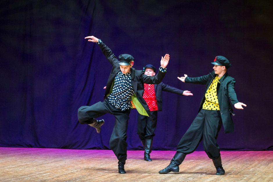 Vibrant folk dance performance by three young male performers on stage.